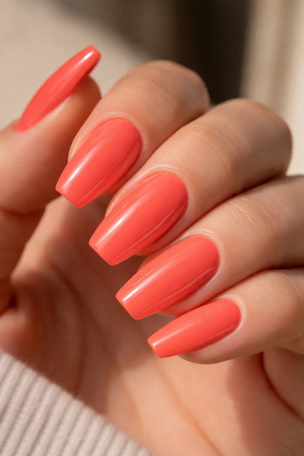 Close-up of electric coral nails with glassy finish