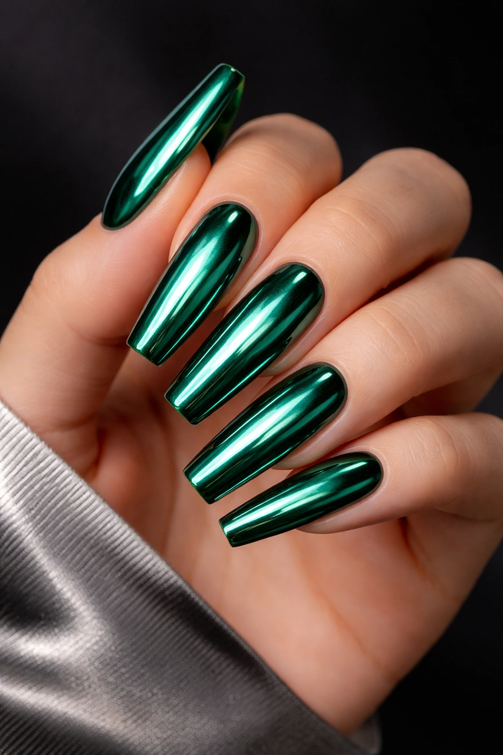 Close-up of coffin-shaped emerald nails with chrome mirror finish reflecting studio light