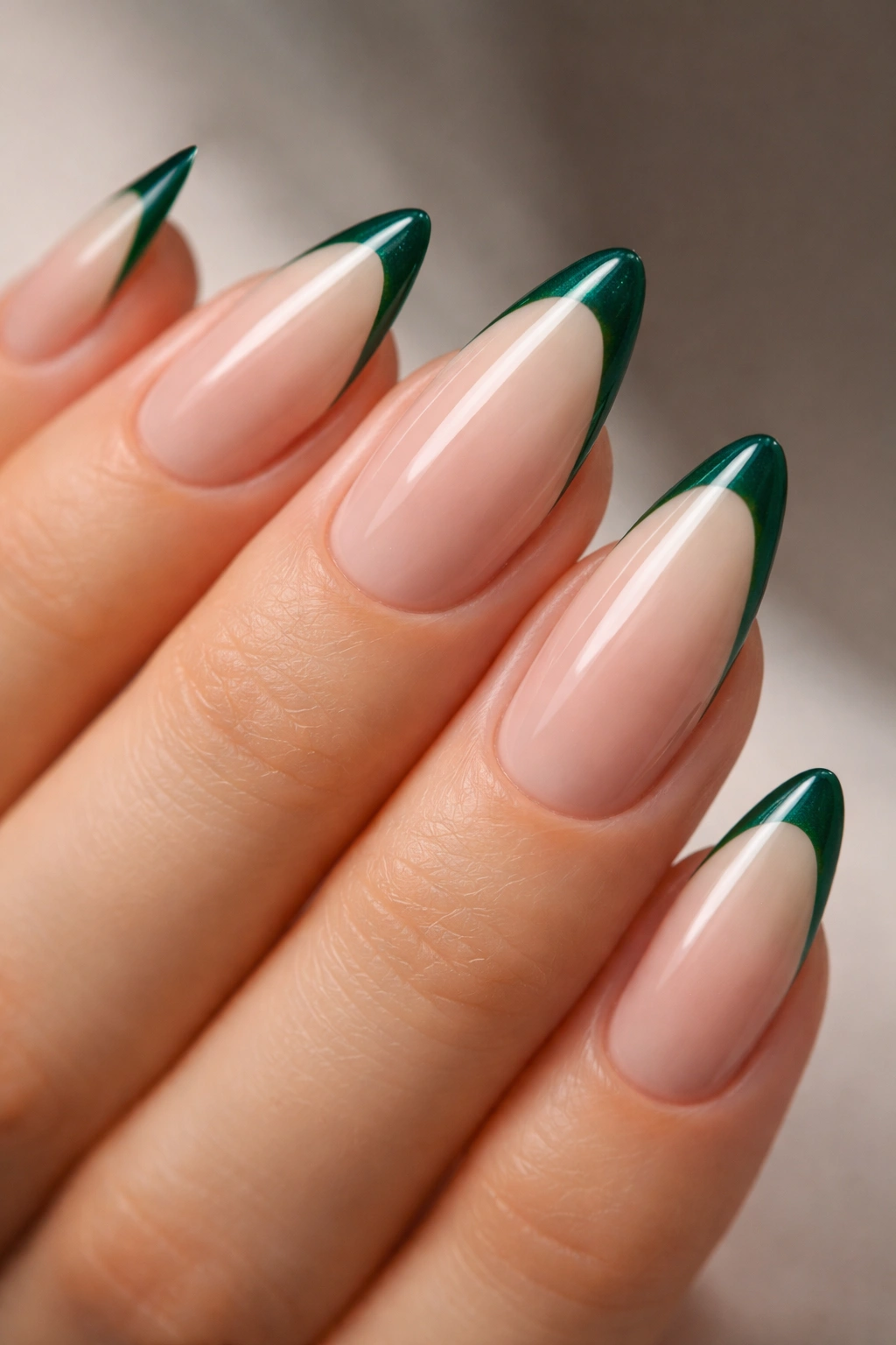 Close-up of almond nails with emerald French tips on a nude base.
