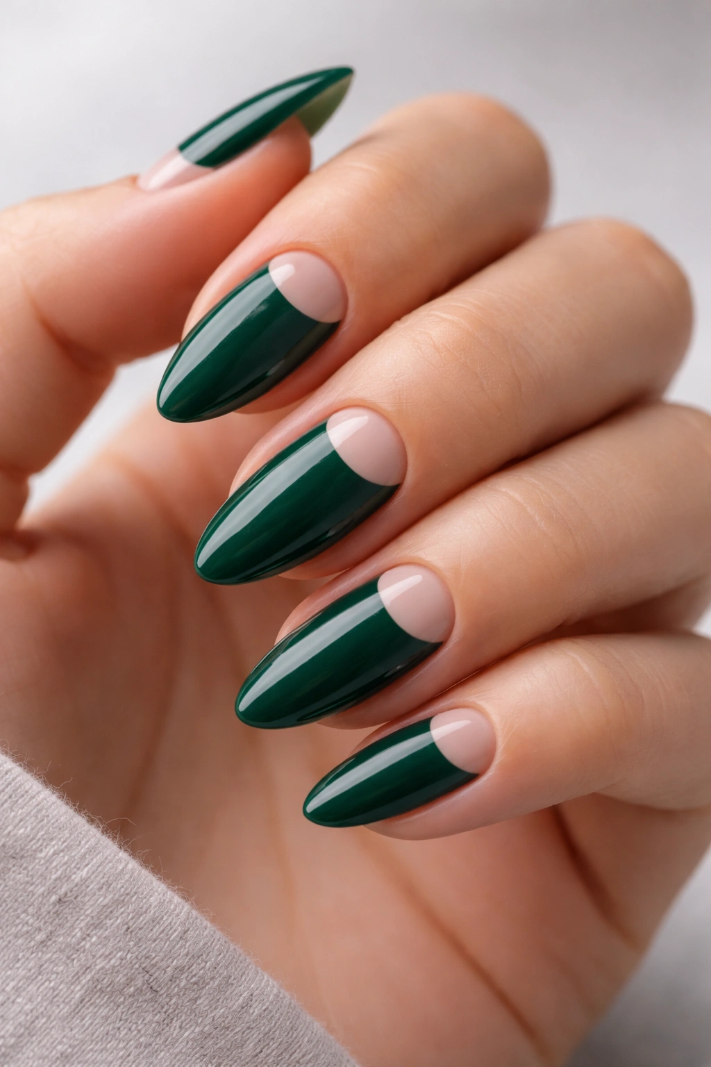 Close-up of almond nails with emerald half-moon negative space design and glossy finish