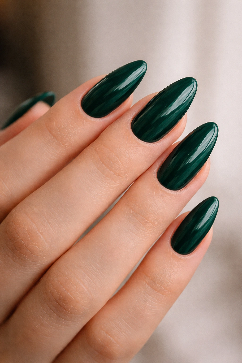 Close-up of glossy emerald almond nails on a neutral background.