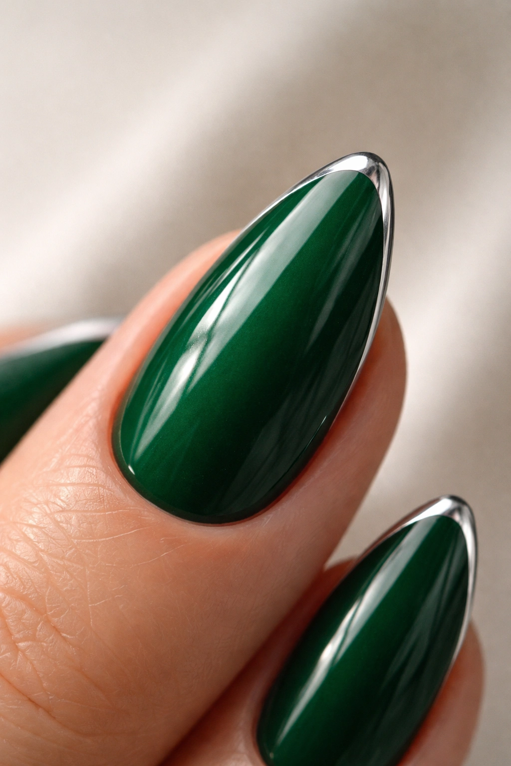 Close-up almond nail with emerald base and thin silver chrome edge