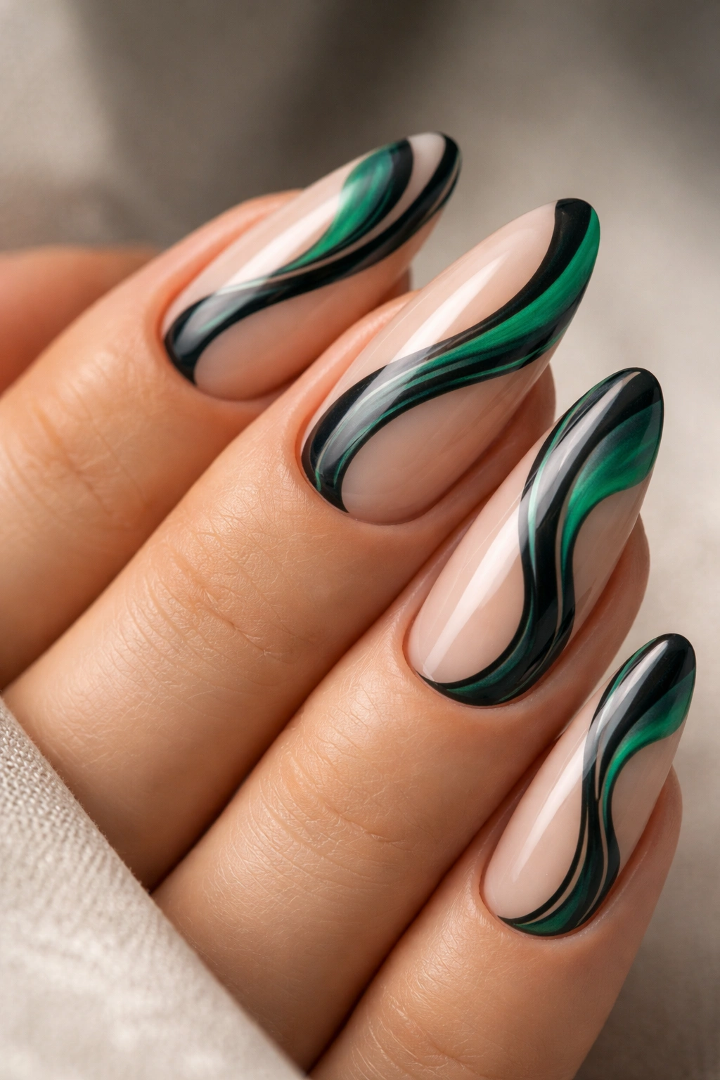 Almond nails with black and emerald swirl patterns on a nude base