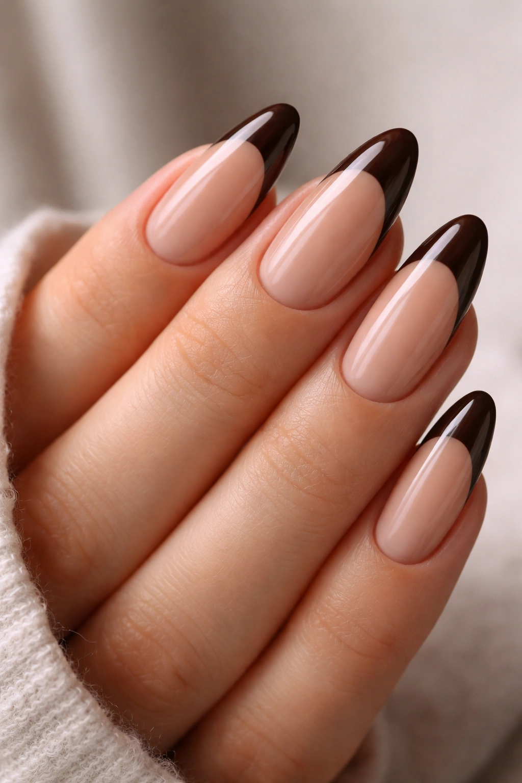 Close-up of almond nails with espresso brown tips on a warm nude base