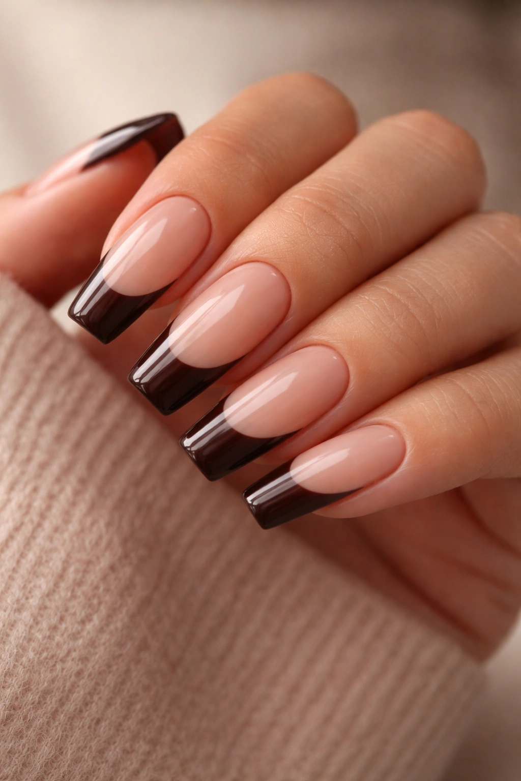 Close-up of medium coffin nails with espresso brown glossy French tips on nude base