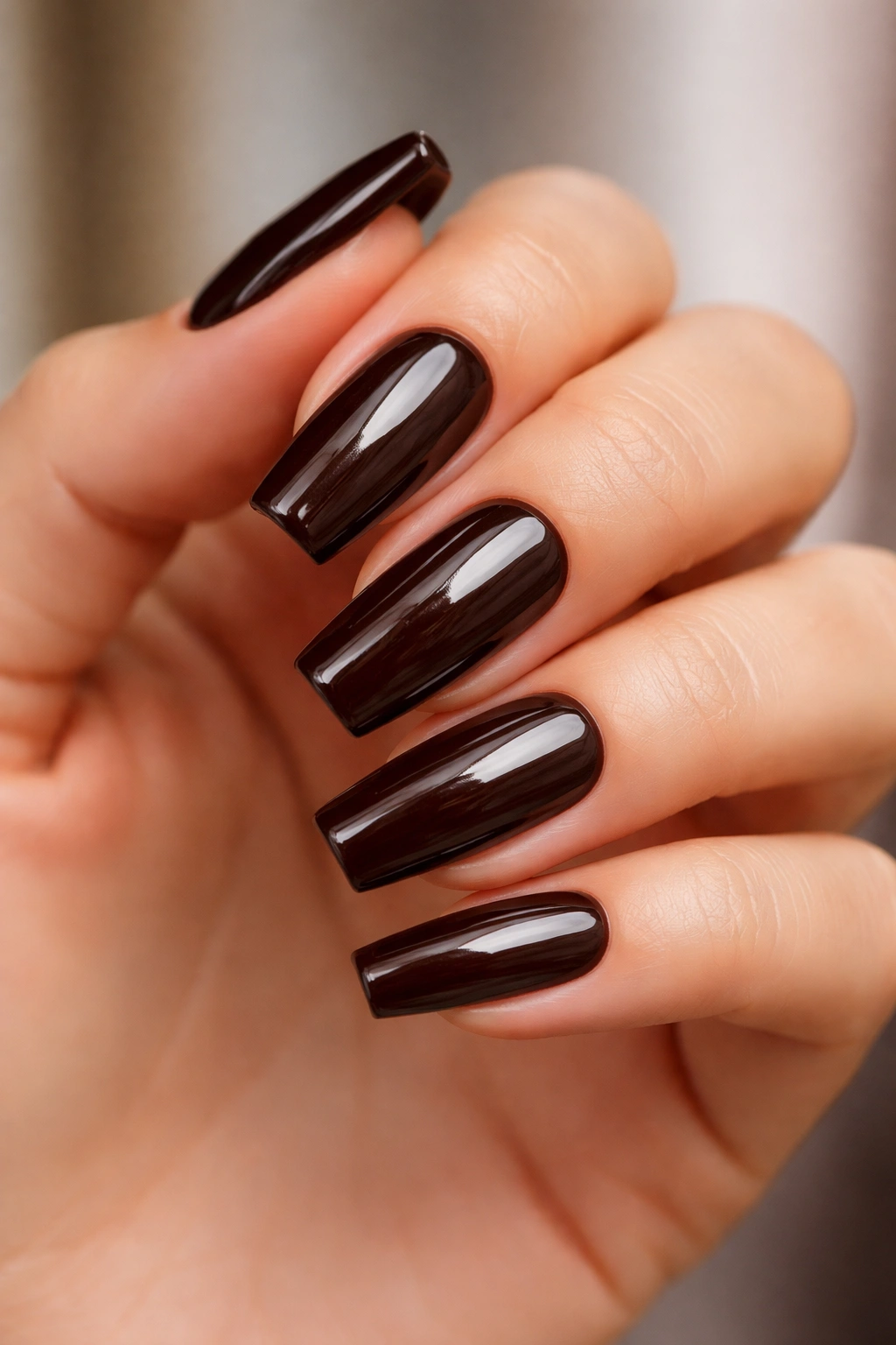Medium-length coffin nails in espresso brown gloss on a hand with neutral skin tone
