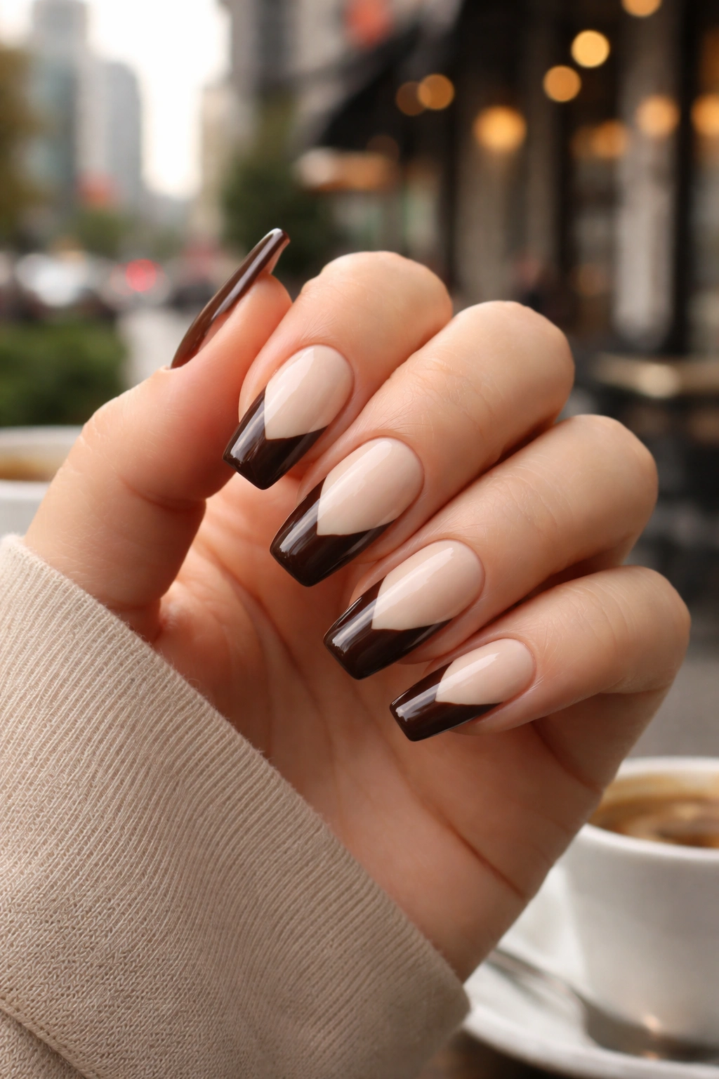 Close-up of espresso and cream coffin nails with diagonal tips on a hand.