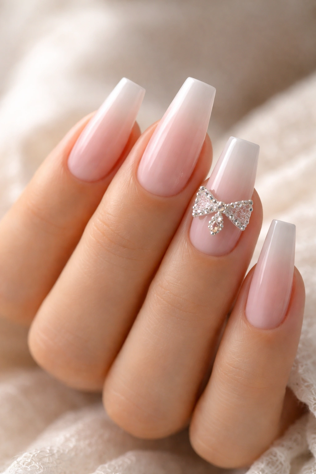 Close-up of French fade coffin nails with crystal bow accent near the cuticle