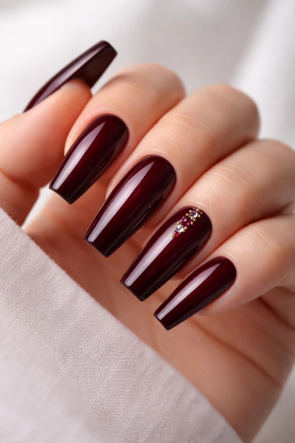 Close-up of garnet rhinestones accenting burgundy coffin nails near the cuticle