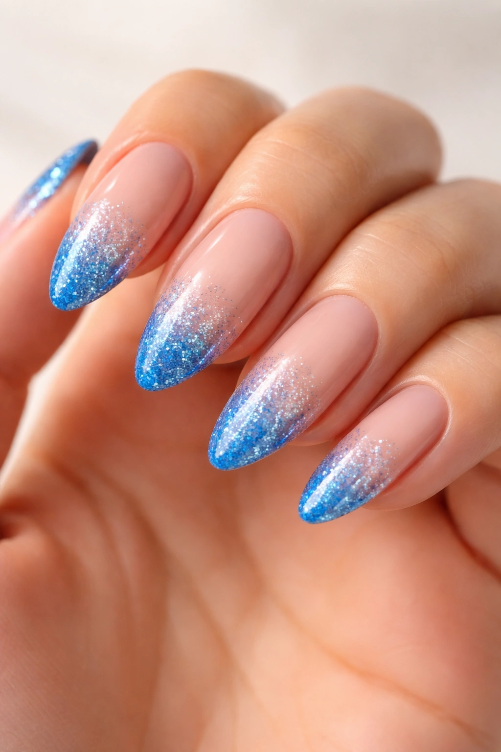 Almond nails with blue glitter tips on a nude base