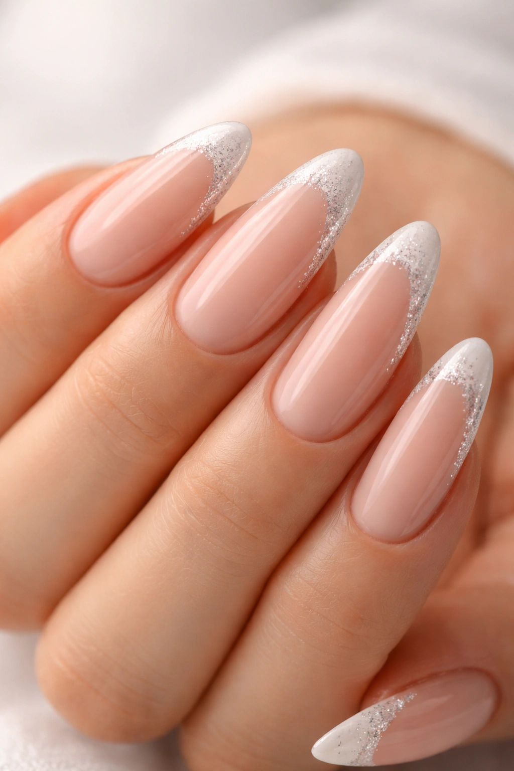 Close-up of long almond nails with a glittery tip on a nude base