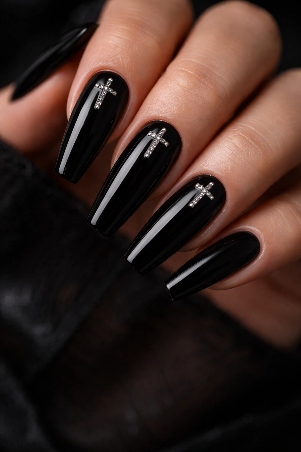 Glossy black coffin nails with small cross charms near cuticle on a hand