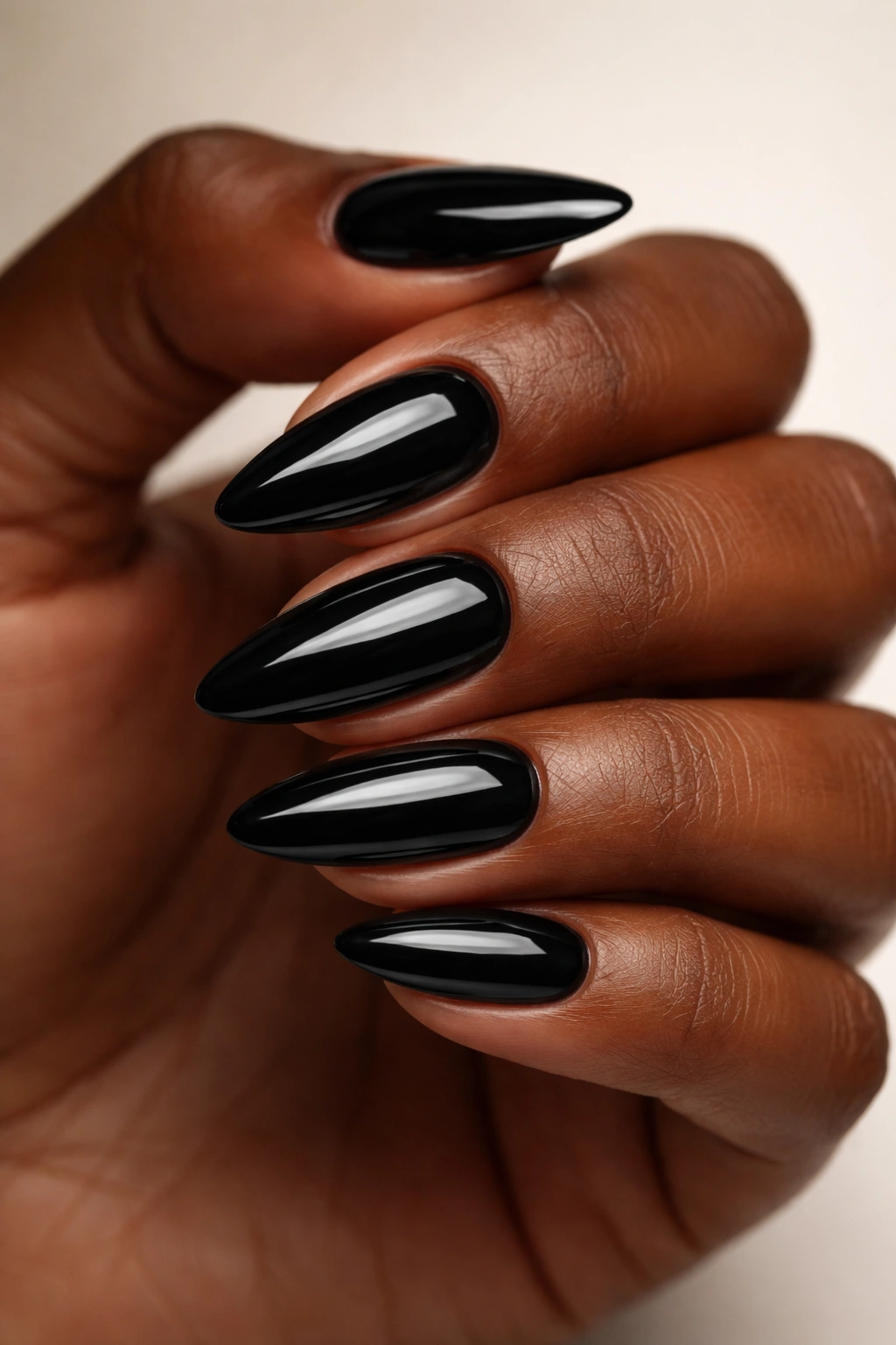 Close up of glossy jet-black almond nails on dark skin