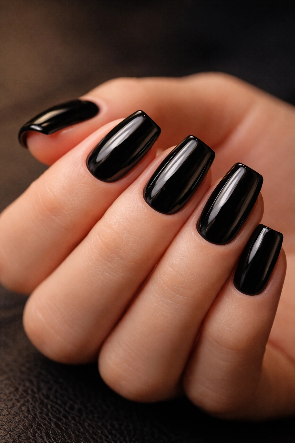 Close-up of glossy black short coffin nails with smooth surface and capped tips.