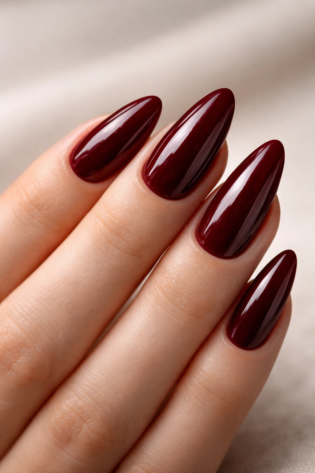 Close-up of almond nails with glossy maroon polish and smooth curved surfaces.