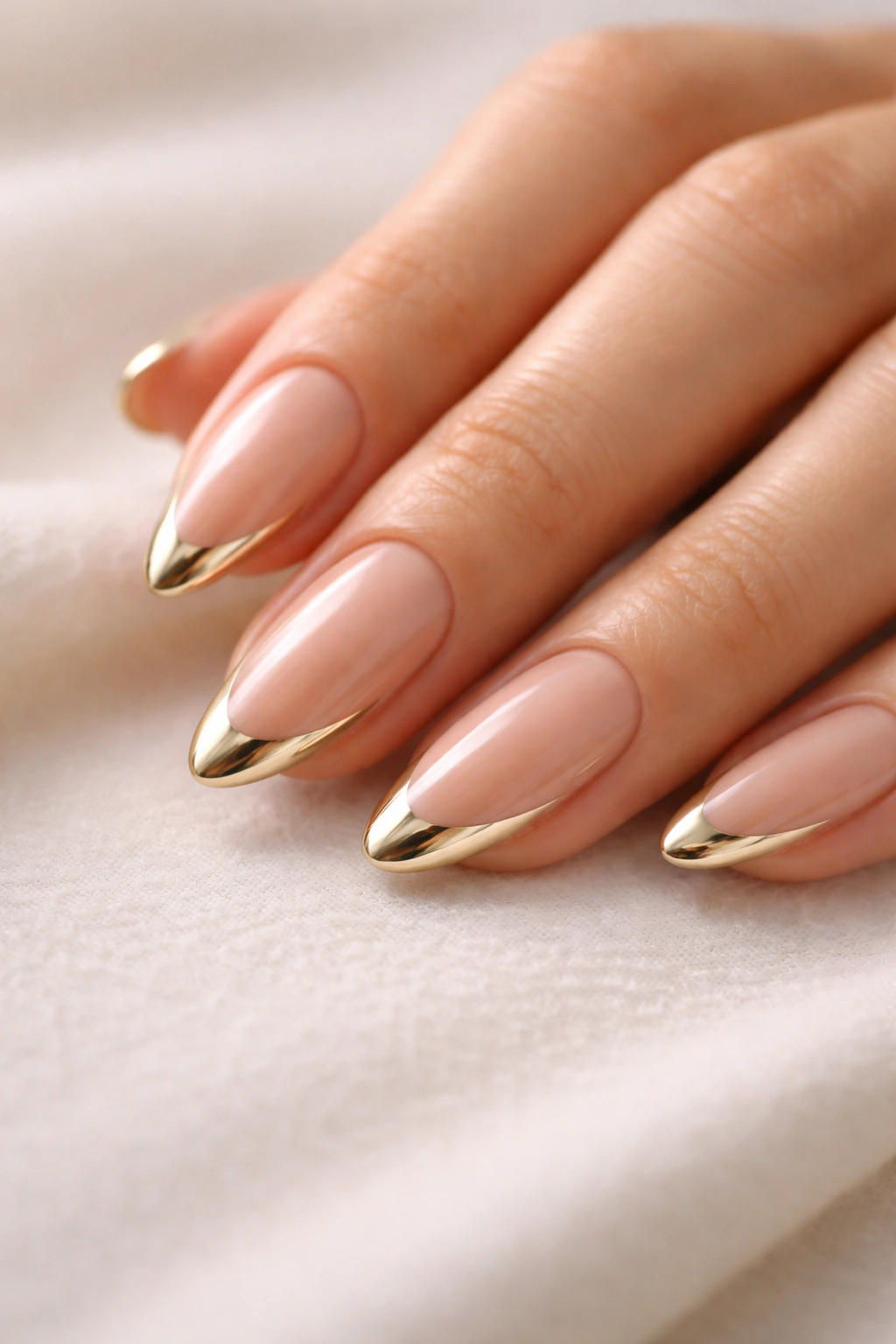 Close-up of almond nails with gold chrome French tips on a neutral base