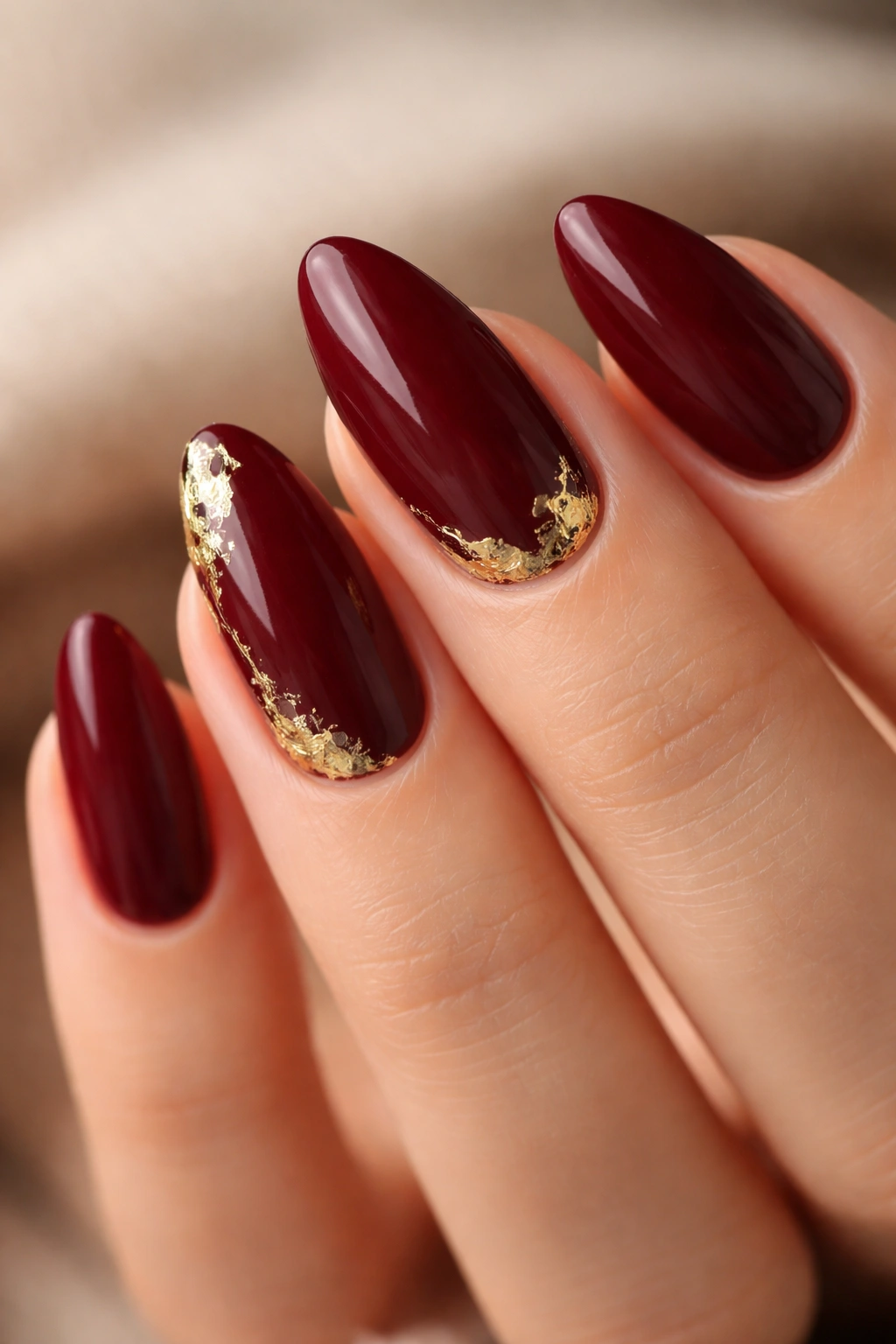 Close-up of maroon nails with gold foil accent on one nail.