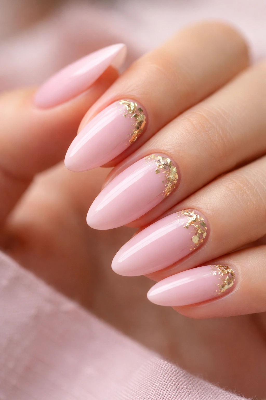 Close-up of soft pink almond nails with gold foil accents