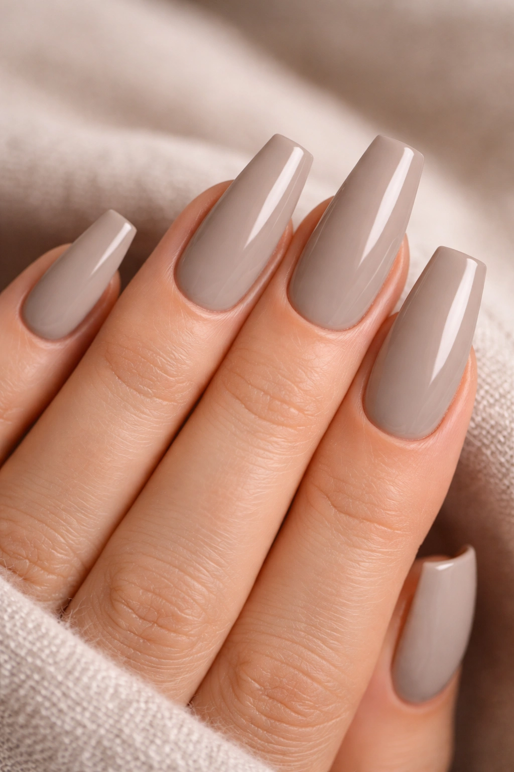 Close-up of greige coffin nails with a glossy finish on a neutral-toned hand