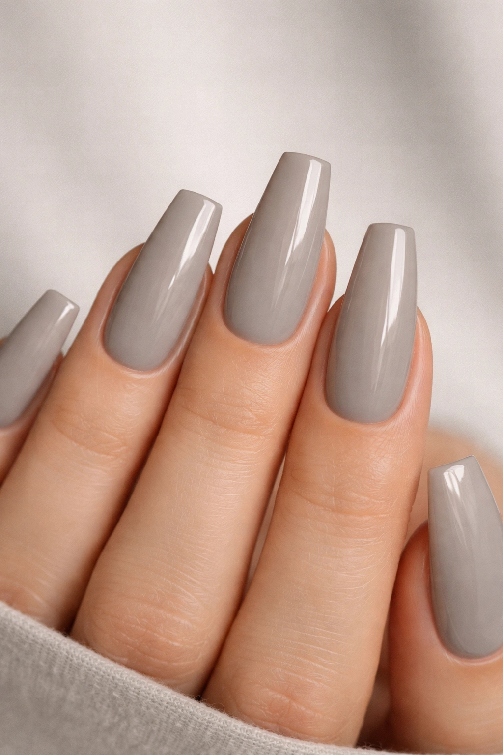 Close-up of cool greige coffin nails with glossy finish on a neutral background