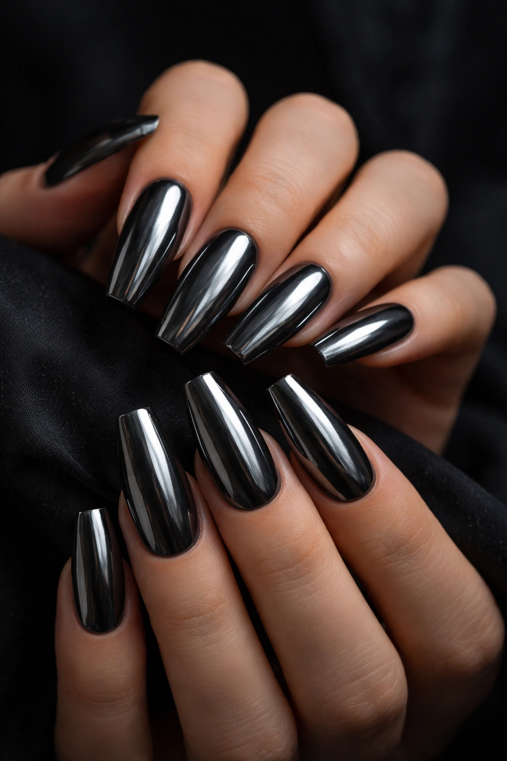 Close-up of ten gunmetal chrome coffin nails on a bare hand with smoky finish in a dark studio