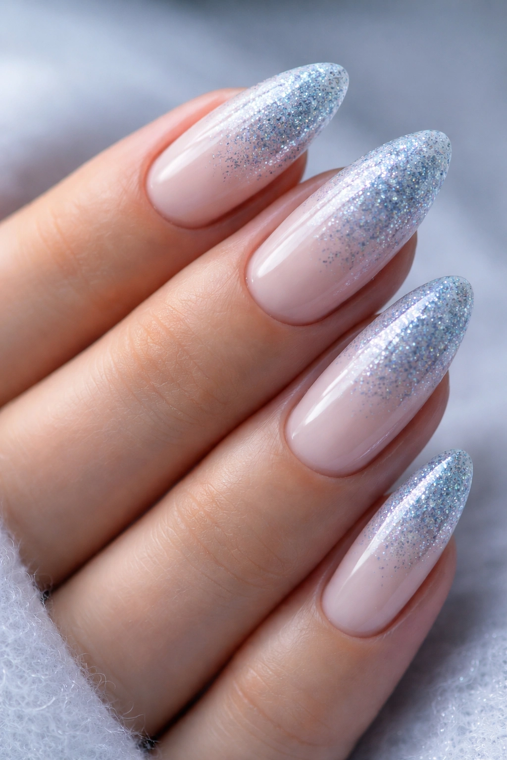 Close-up of icy blue glitter fade on almond nails with milky base