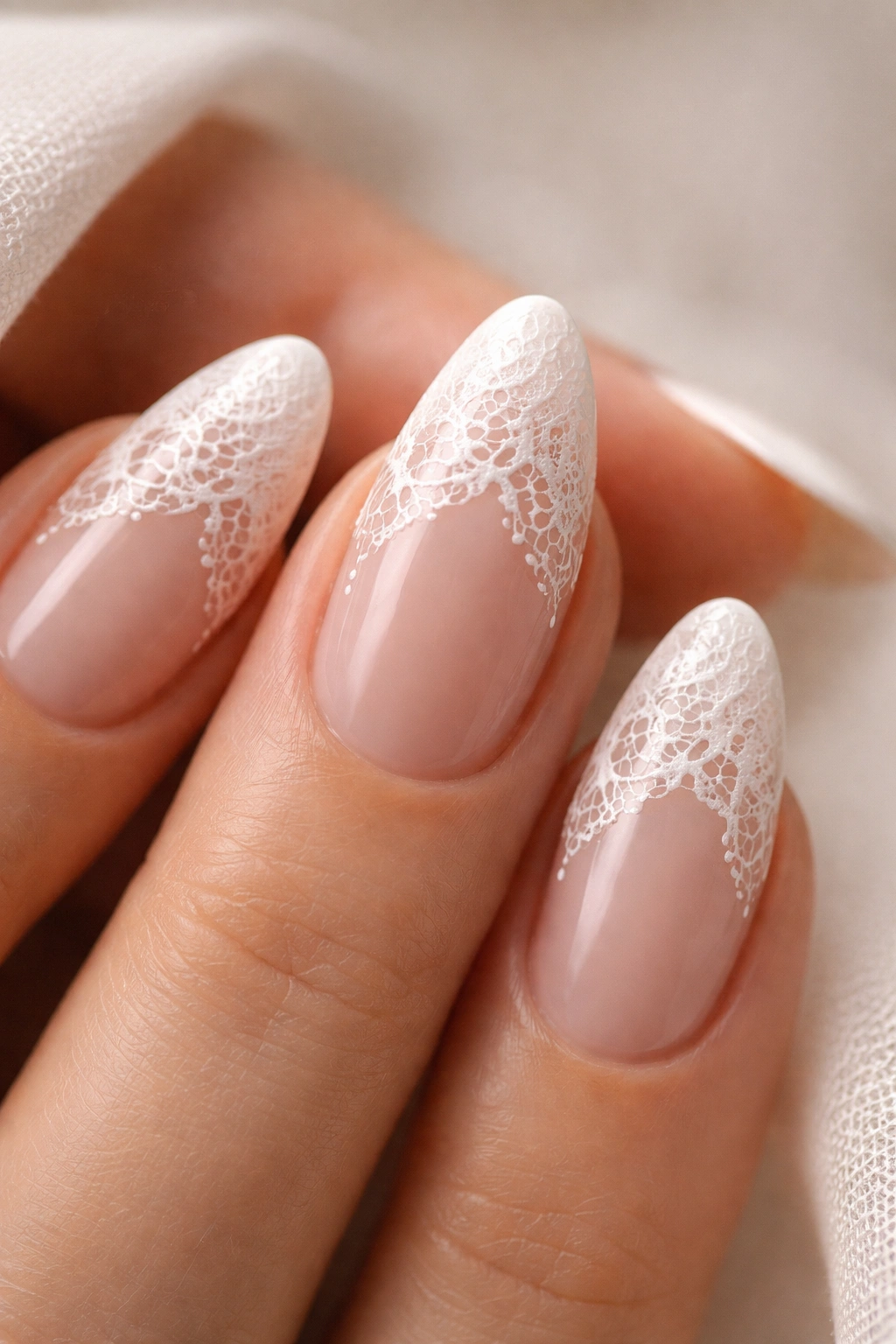 Close-up of almond nails with lace-inspired white detail on nude base