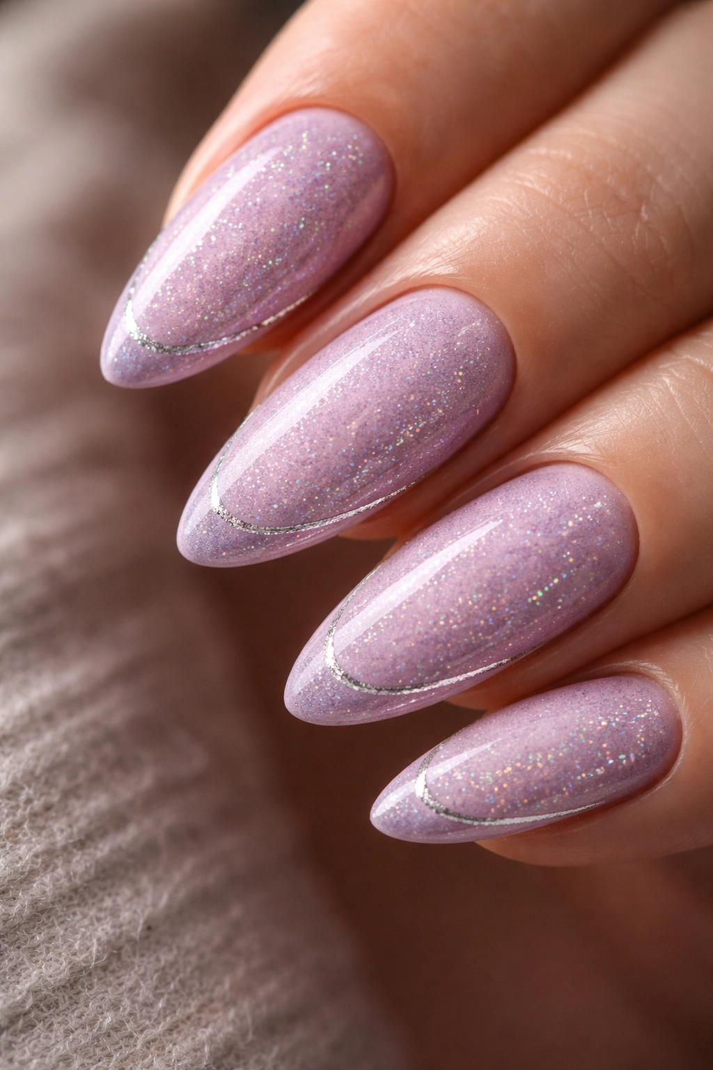 Close-up of almond nails with lilac base and fine silver holographic glitter on a neutral background