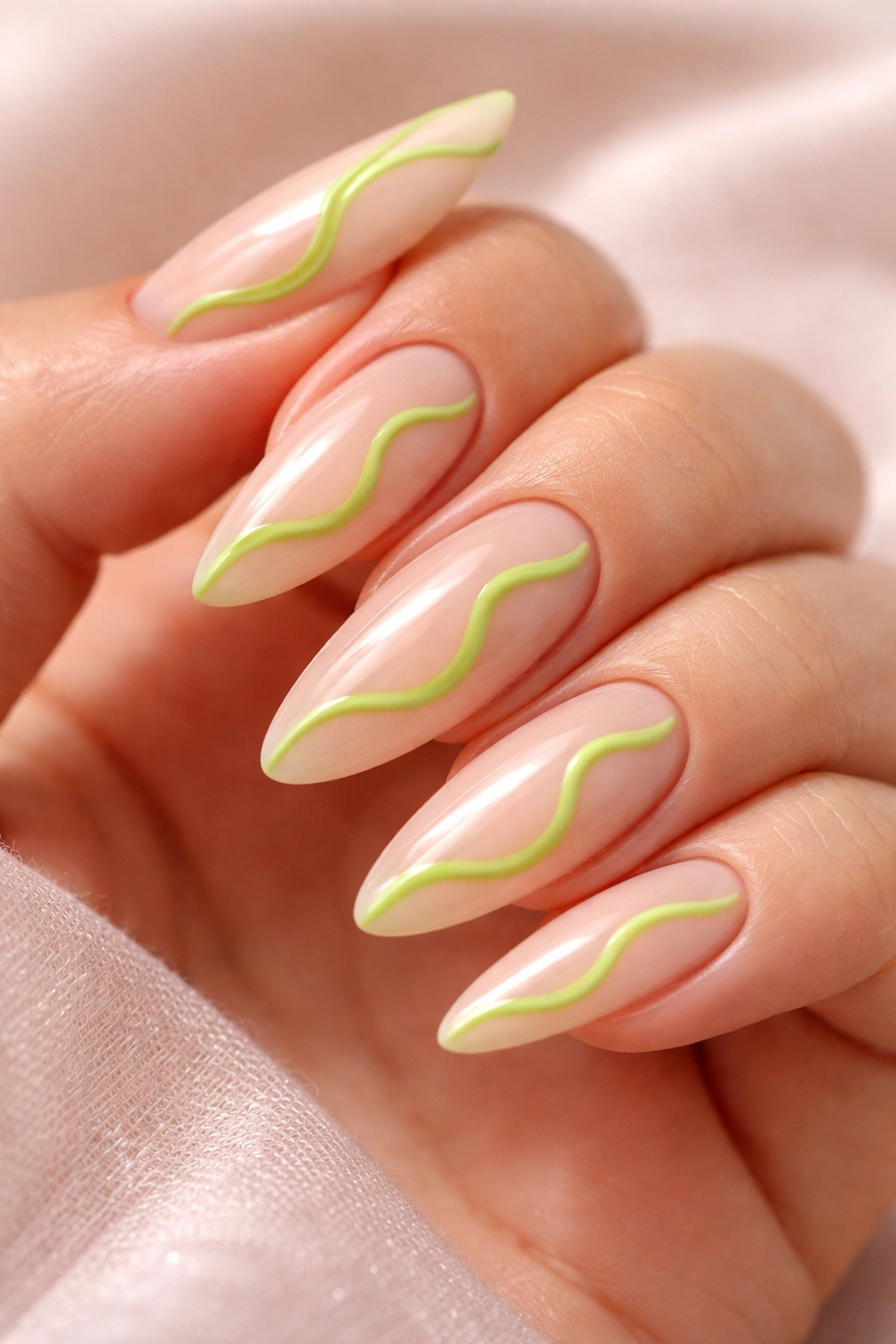 Close-up of almond nails with lime green squiggle on milky base
