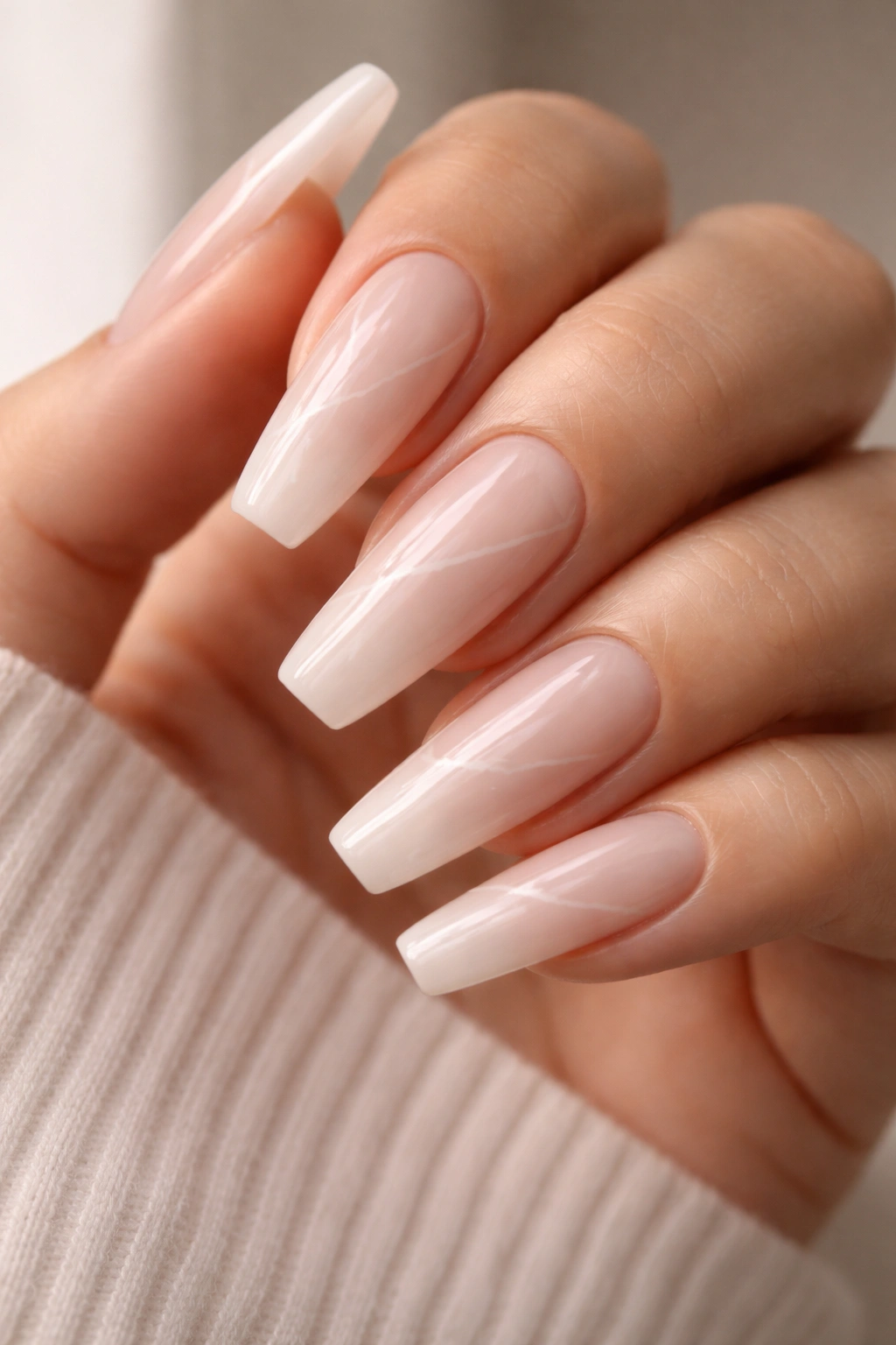 Close-up of bare hand with soft milky pink marble coffin nails and thin white veins.