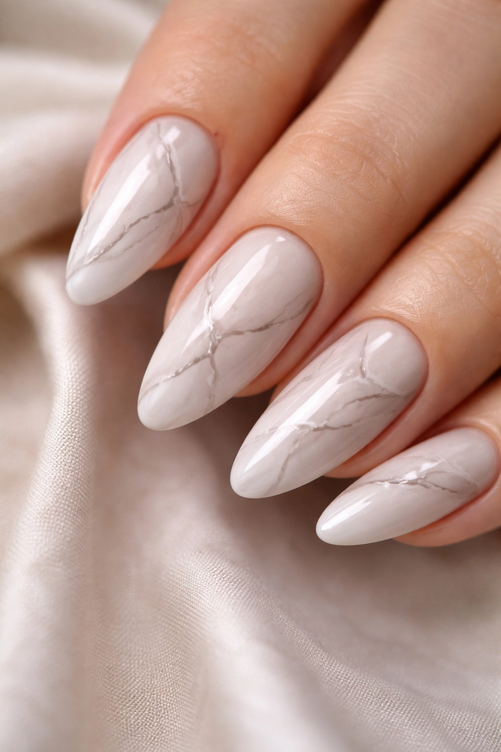 Almond nails with delicate white marble veins on a pale nude base