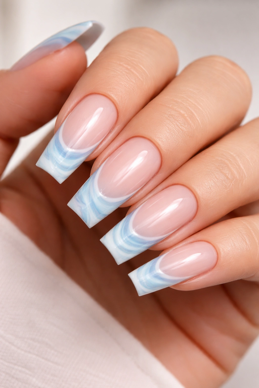 Close-up of coffin nails with marble swirl light blue French tips on a nude base