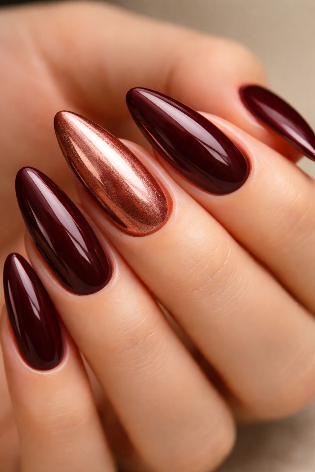Almond nails with deep maroon base and copper rose-gold chrome accent on select nails