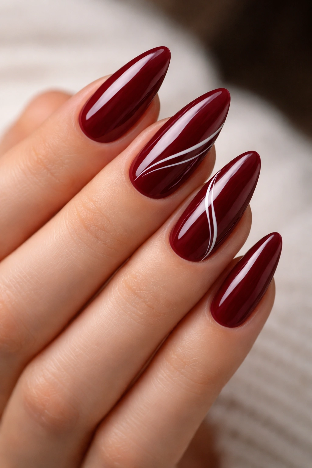 Almond nails in maroon with thin white swirl accents on one or two nails
