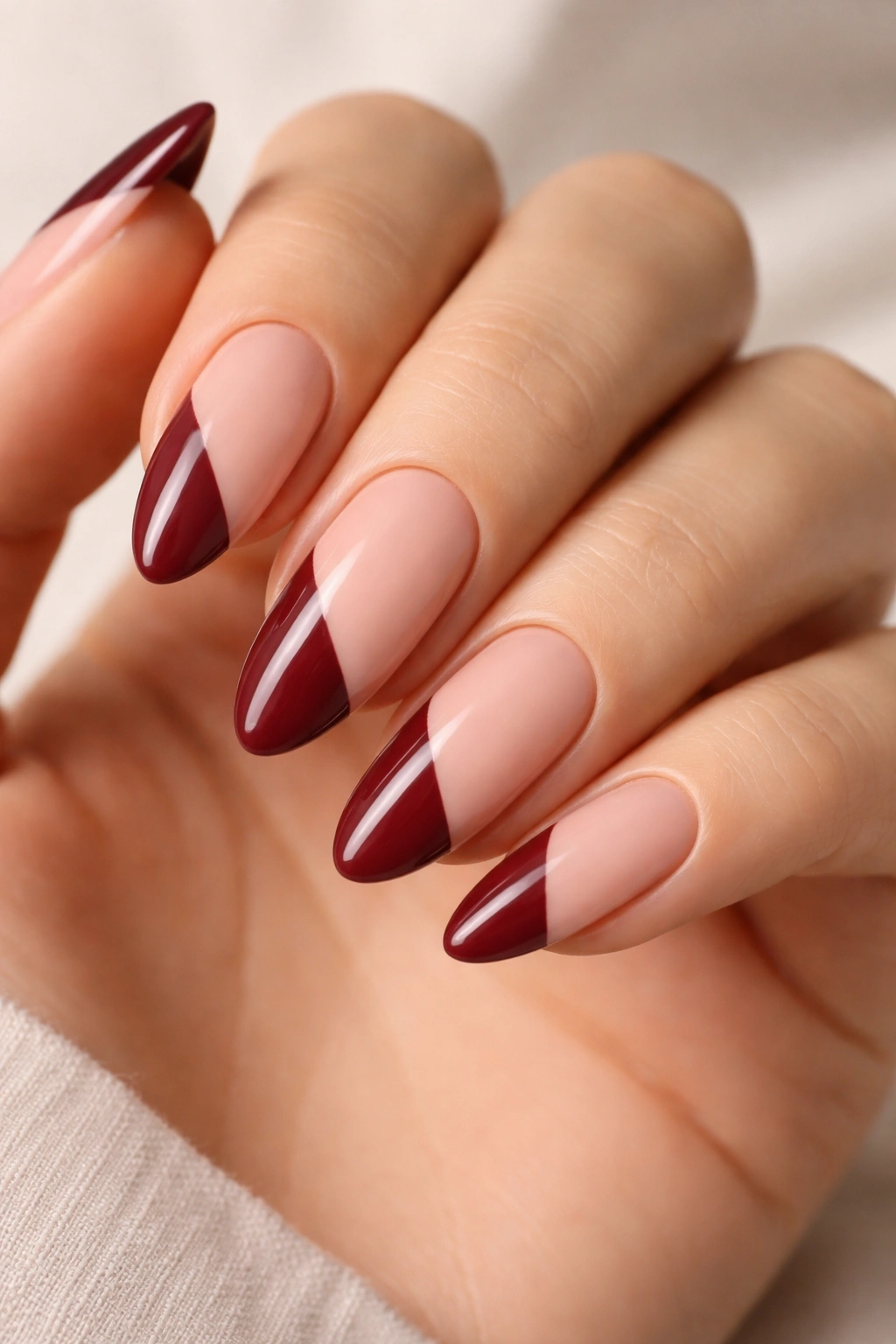 Close-up of almond nails with maroon color-block against nude space.