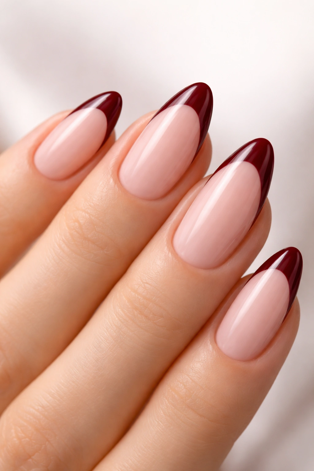 Close-up of almond nails with sheer pink base and maroon French tips.