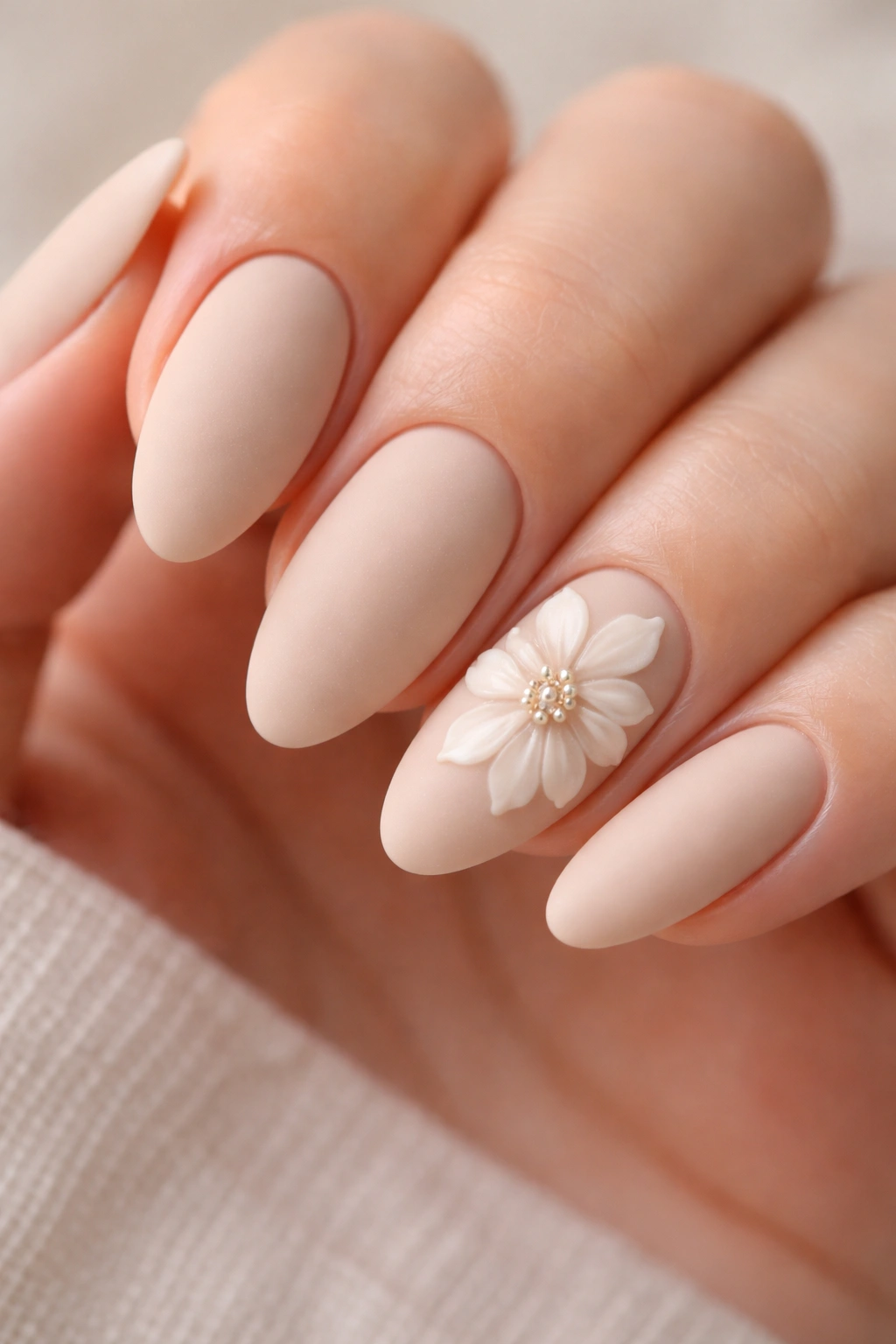 Matte beige almond nails with raised 3D gel petals on an accent nail