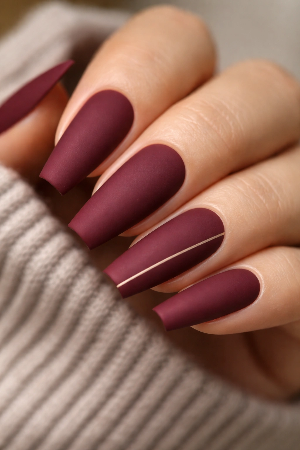 Close-up of matte burgundy coffin nails with a thin gold accent line near the cuticle