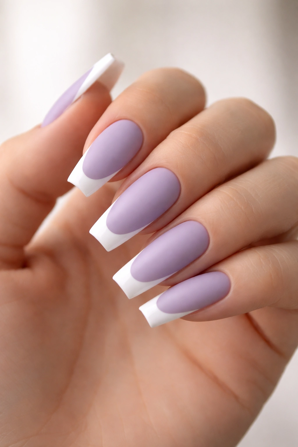 Close-up of matte lavender coffin nails with glossy French tips on a hand