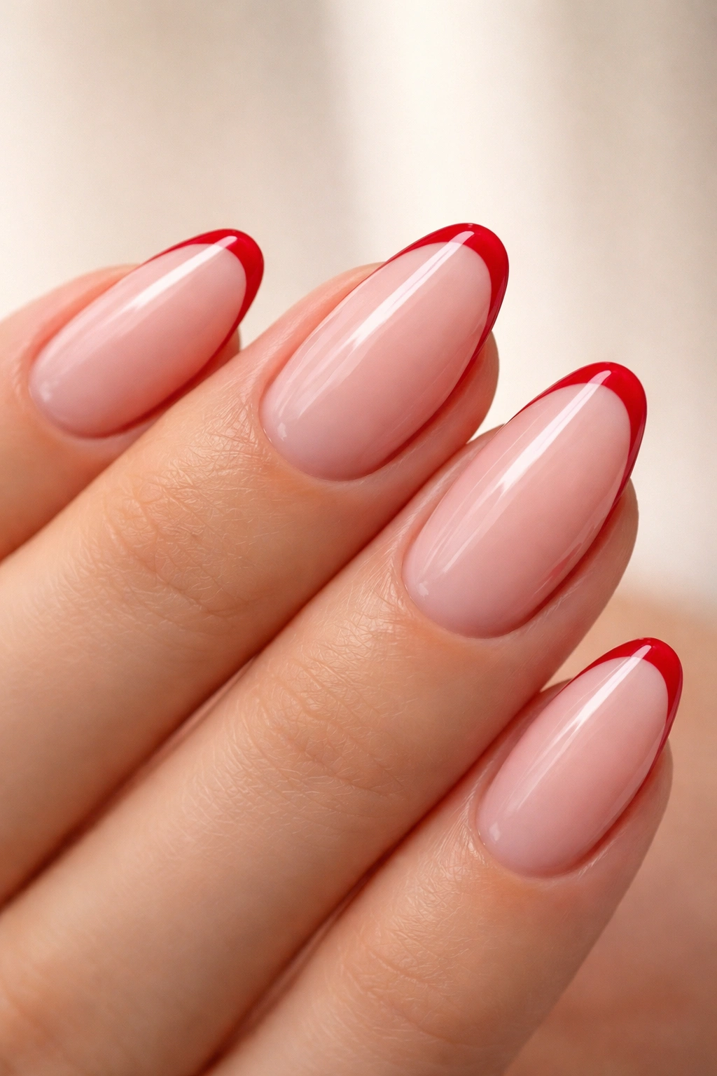 Close-up of soft almond nails with micro cherry red French tips on a sheer pink base