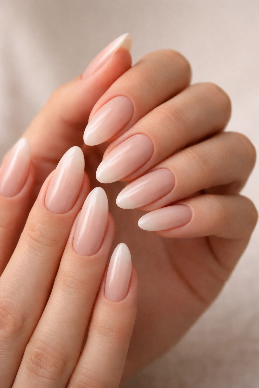 Close-up of almond nails with a sheer milky pink base on a neutral background