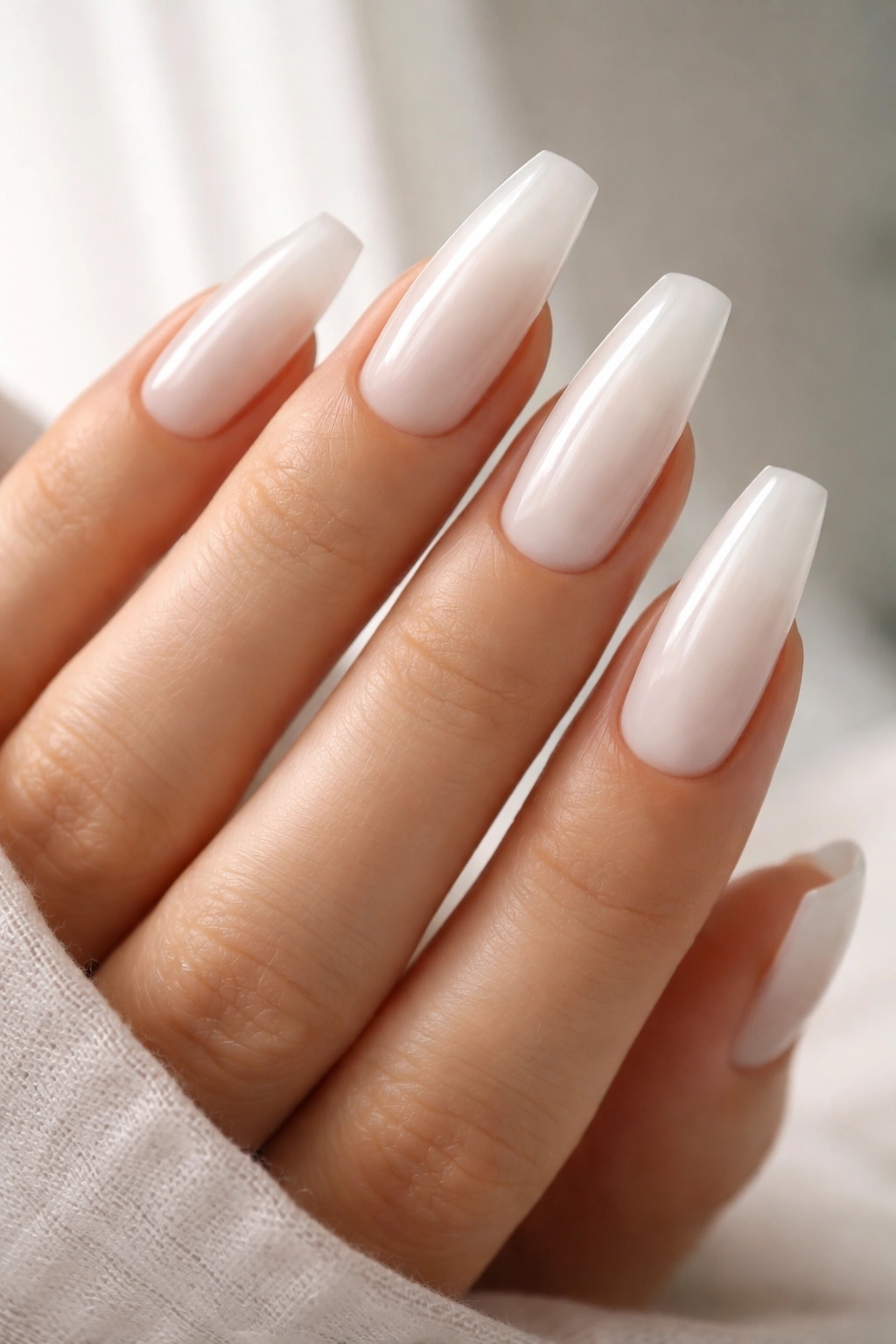 Milky white coffin nails with translucent finish on a hand