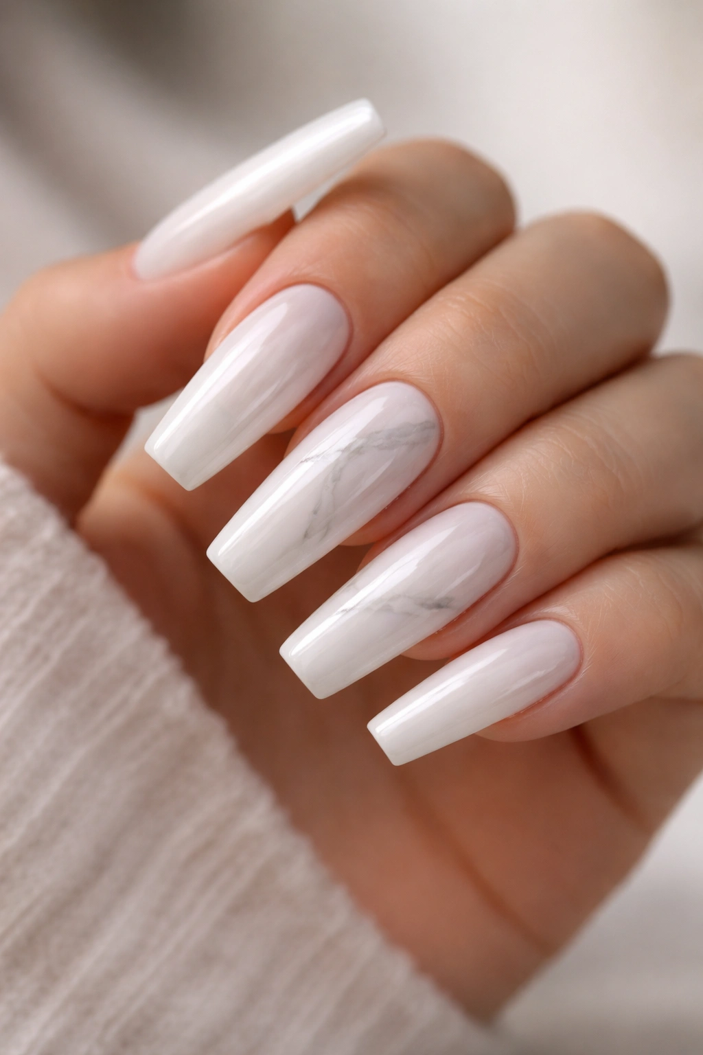 Close-up of milky white coffin nails with soft gray marble veining on a neutral-toned hand