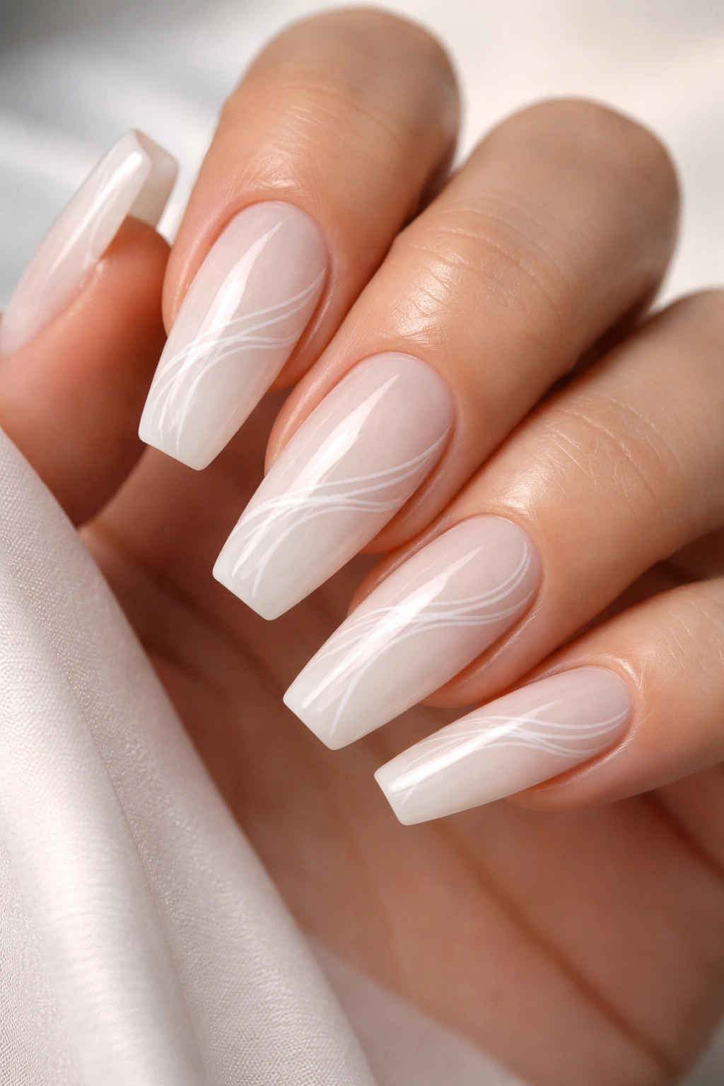 Close-up of milky coffin nails featuring a delicate white swirl overlay