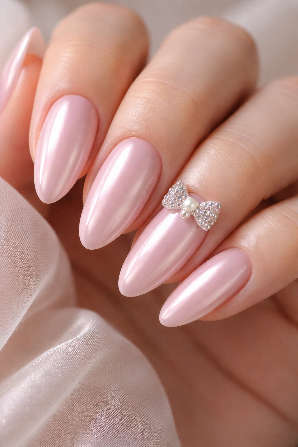Milky pink chrome nails with a small 3D bow charm on an accent nail