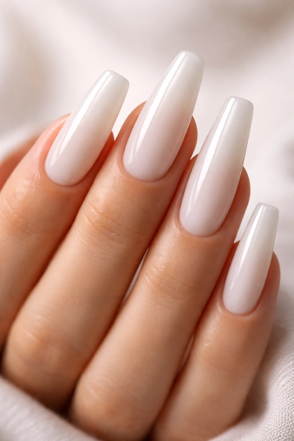 Close-up of milky white coffin nails with soft glow on a neutral backdrop