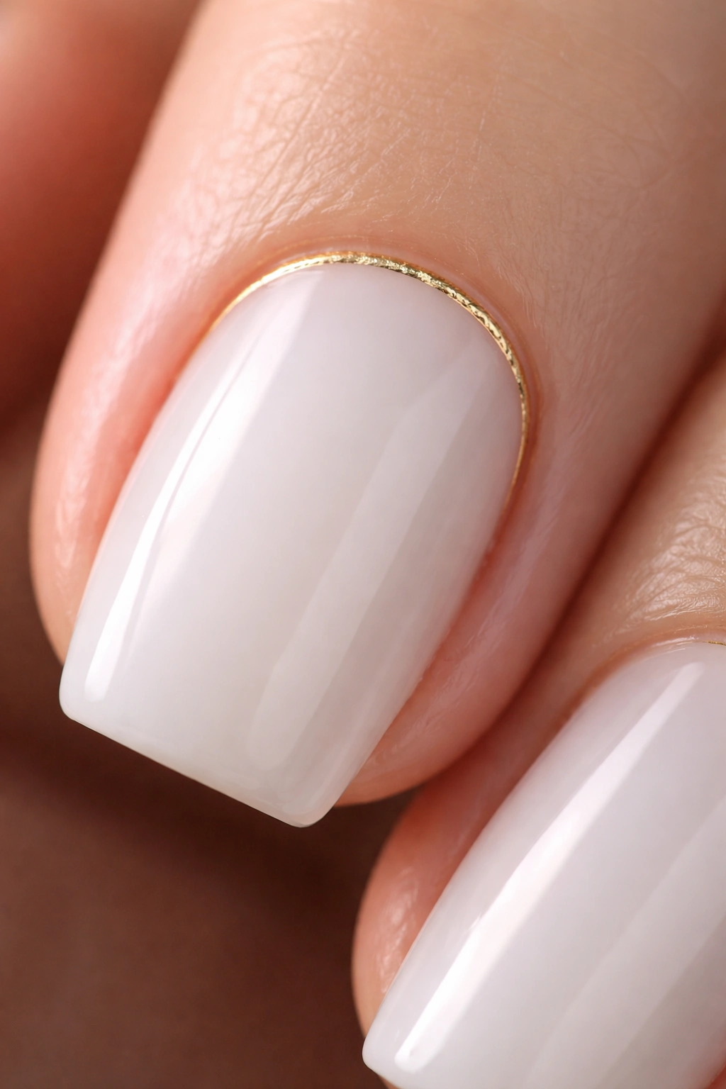 Close-up of a short coffin nail with milky white base and a thin gold cuticle cuff