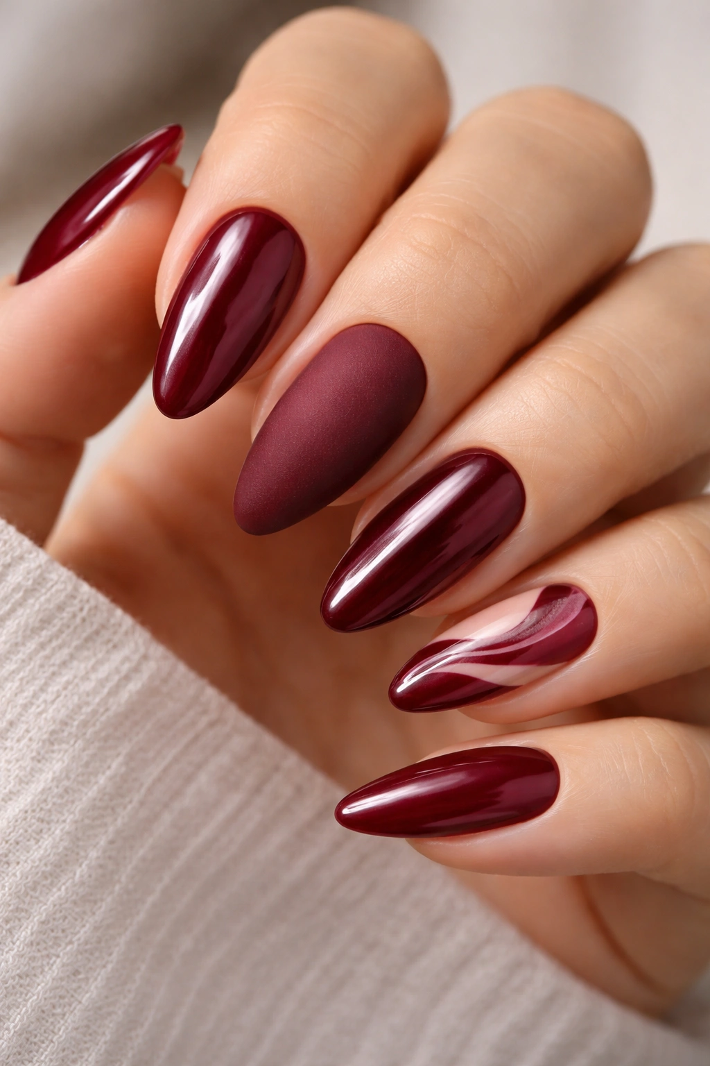 Almond nails showing mixed finishes in a maroon palette: glossy, matte, chrome, French tip, and swirl