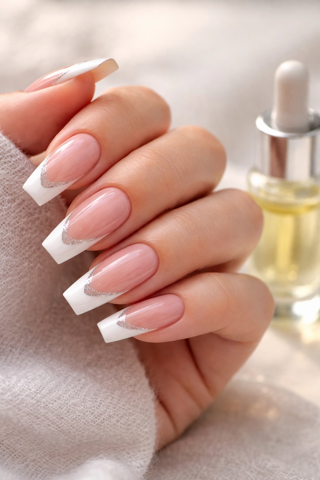 Close-up of a hand with modern French tip coffin nails and cuticle oil nearby.