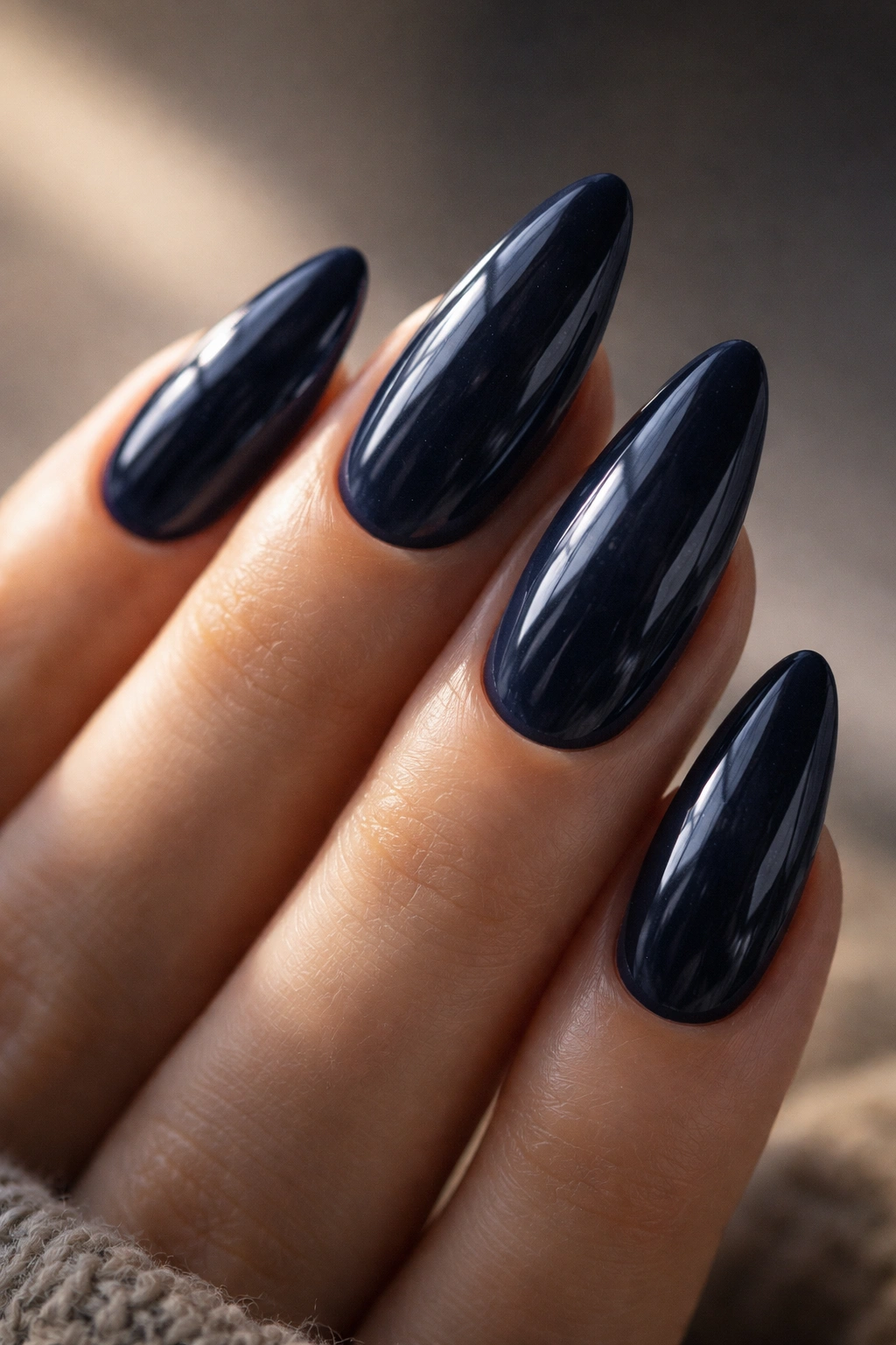 Close-up of midnight navy almond nails on gel extensions with a glassy finish